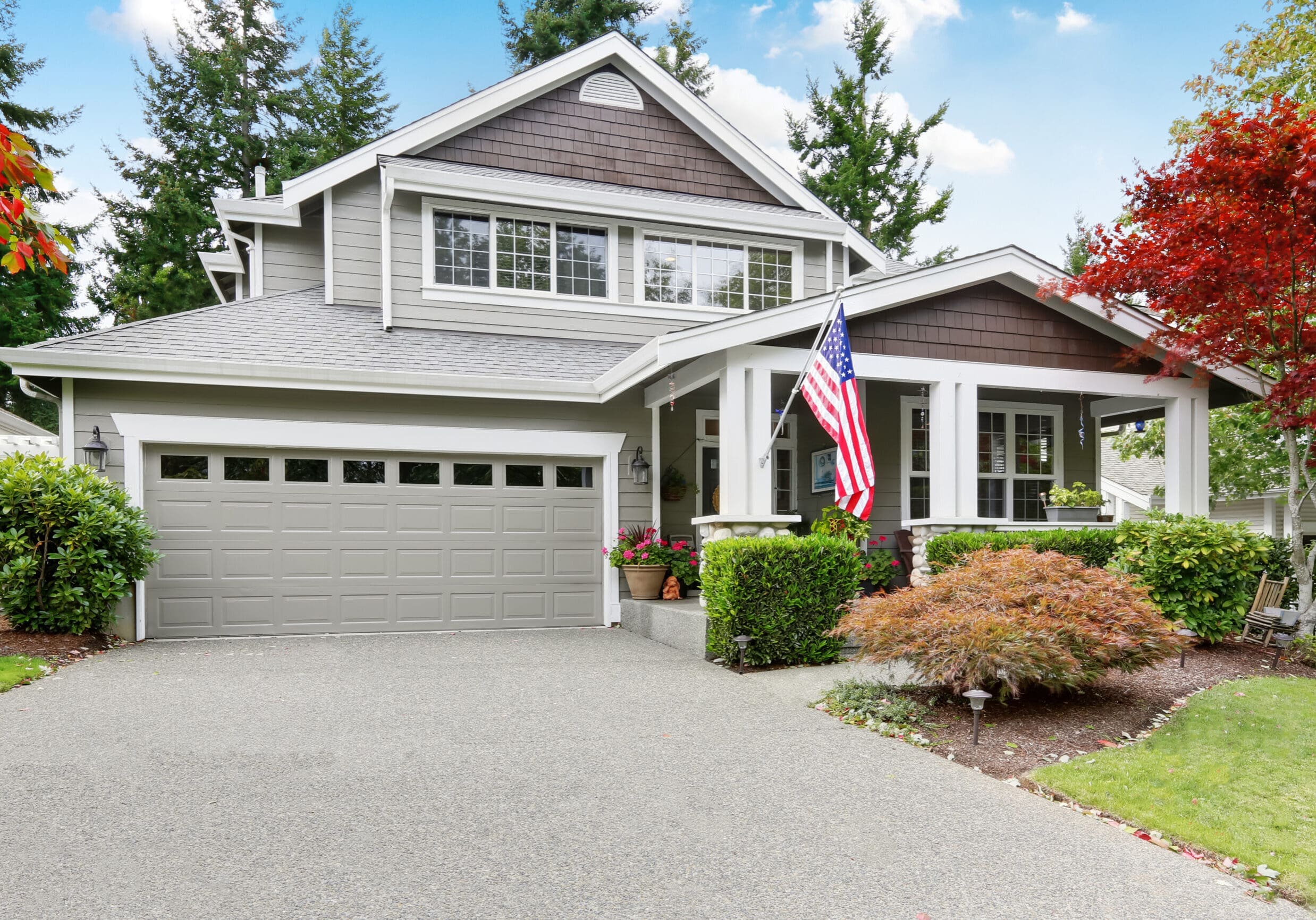 Nice curb appeal of grey house with garage and driveway. Column porch with American flag. Northwest, USA